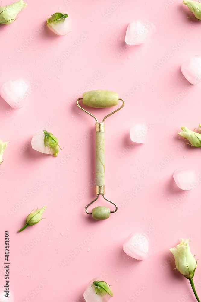 Green jade stone face roller top view on pink background with ice cubes and flowers. Green jade stone face roller top view on pink background with ice cubes and flowers.