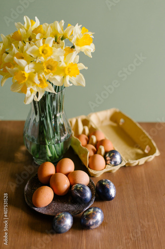 Beautiful festive Easter still life. A bouquet of daffodils in a glass vase and painted eggs are on the table. Spring mood. Colorful minimalistic postcard. Flowers yellow narcissus springtine photo