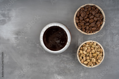 Three cups with different stages of coffee: green and roasted beans and ready drink. On gray background