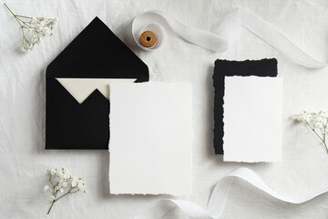 Wedding invitations mockups and black envelopes on textile background with flowers and white ribbon. Elegant wedding flat lay composition. Top view.