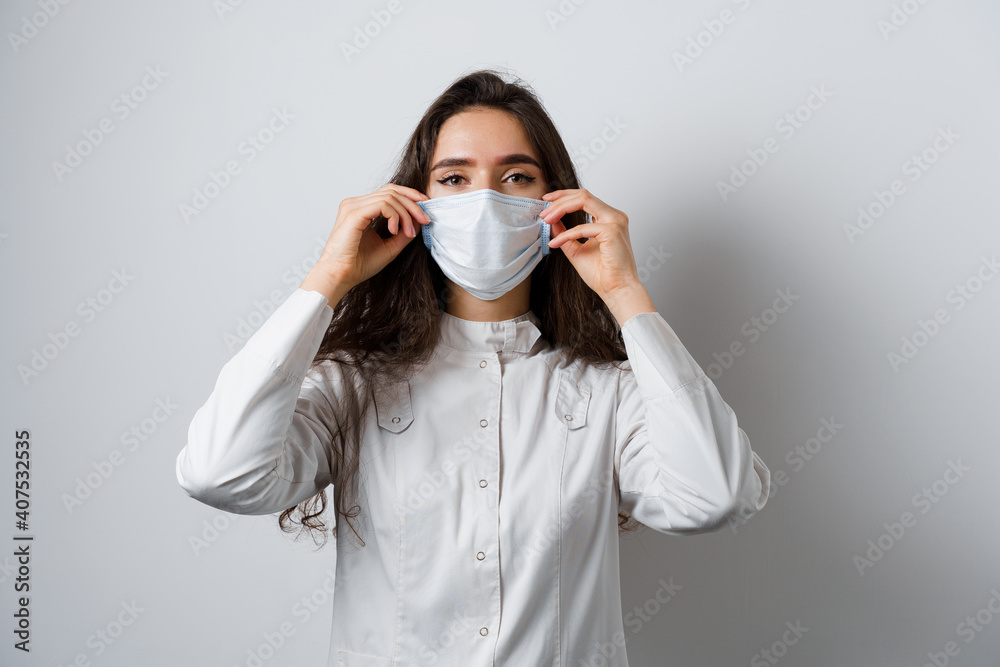 Doctor wearing medical mask on white background. Young attractive woman in medical robe. Quarantine coronavirus covid-19 trends. Doctor wearing medical mask on white background. Young attractive woman in medical robe. Quarantine coronavirus covid-19 trends.