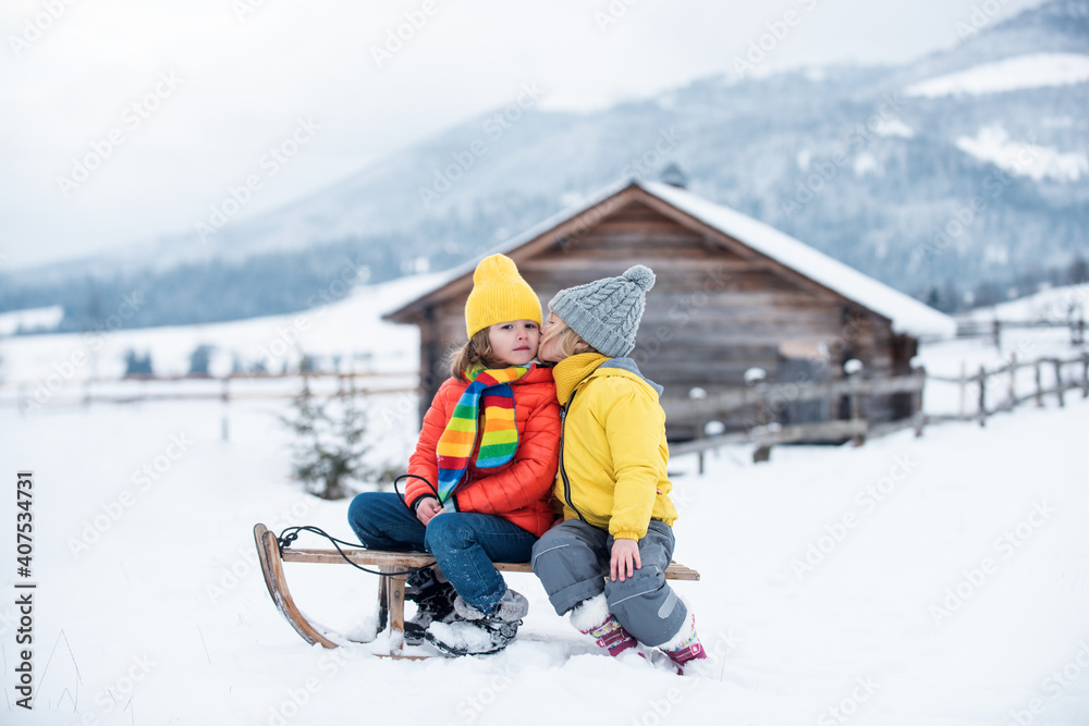 Winter kids Picnic. Romantic little couple sitting on sled in snow, hugging and kissing. Enyoying holiday season, spending time outdoors together Children friends kiss.