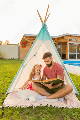 Father reading a story to his daughter while camping in the backyard © Impact Photography