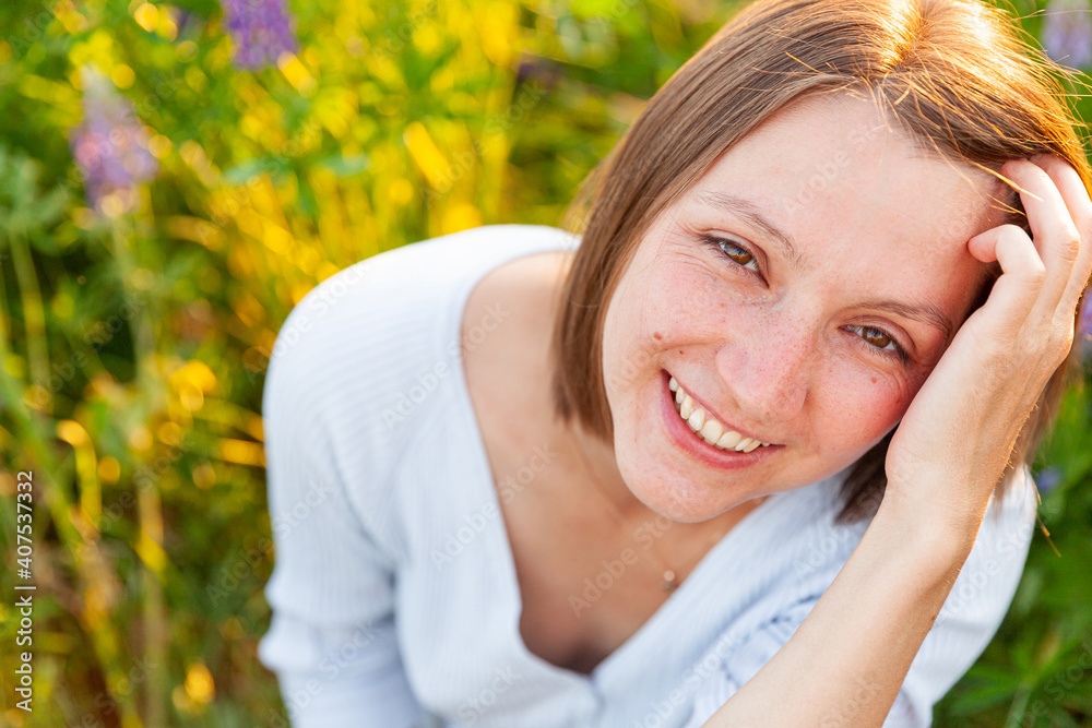 Happy girl smiling outdoor. Beautiful young brunete woman resting on summer field with blooming wild flowers green background. Free happy european woman. Positive human emotion facial expression.