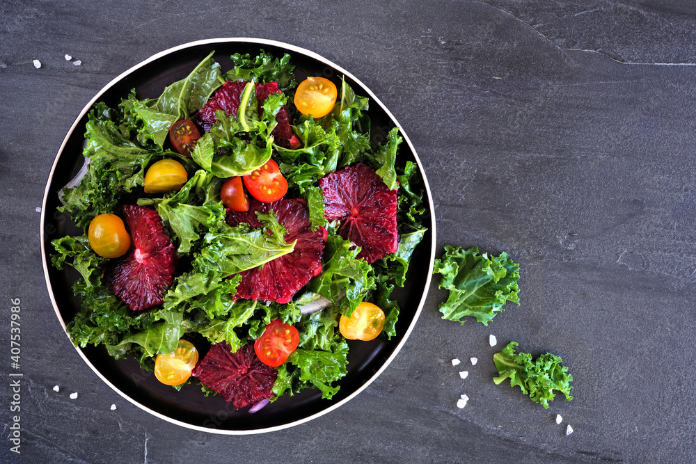 Healthy salad with kale and red blood oranges. Top view over a dark slate background.