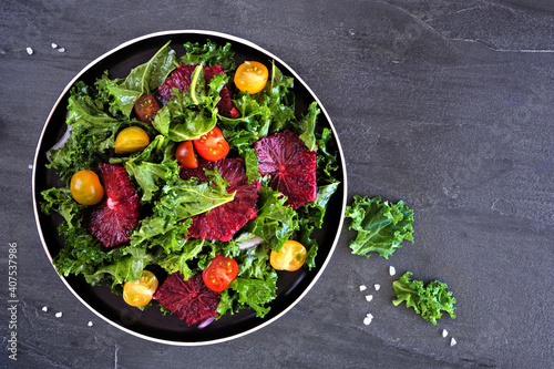 Healthy salad with kale and red blood oranges. Top view over a dark slate background.
