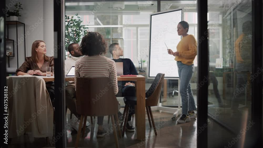 Project Manager Makes a Presentation for a Young Diverse Creative Team in Meeting Room in an Agency. Colleagues Sit Behind Conference Table and Discuss Business Development, User Interface and Design.