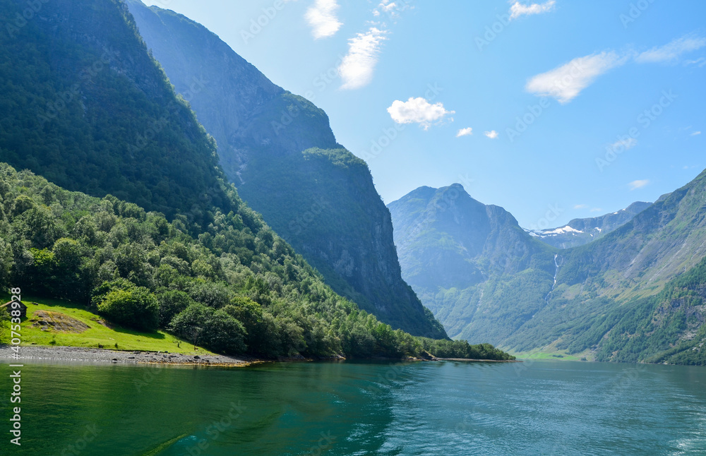 Mountains waterfall and fjord  Sognefjord in Norway. Clouds and blue sky. Beautiful stunning views of mountains, water, sky, clouds and sun. Norwegian nature 
