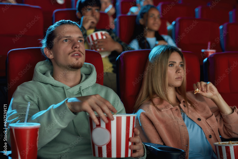 Young couple having popcorn while watching movie together, sitting in cinema auditorium
