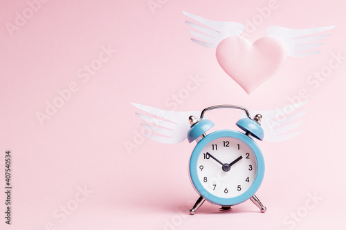 flying heart symbol near alarm clock over pink background. love and romance concept. valentine day greeting card conceptual