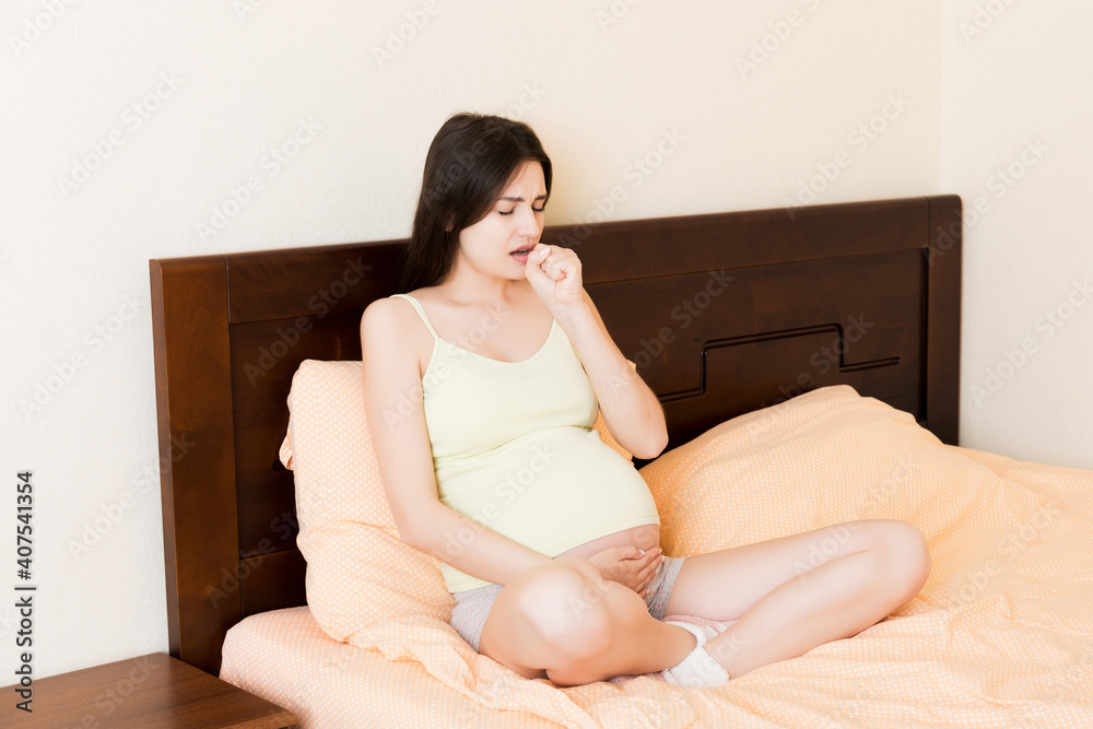 Portrait of young unhappy pregnant woman leaning on pillows on bed and blowing her nose into tissue. Future mom caught cold and sneezing Portrait of young unhappy pregnant woman leaning on pillows on bed and blowing her nose into tissue. Future mom caught cold and sneezing