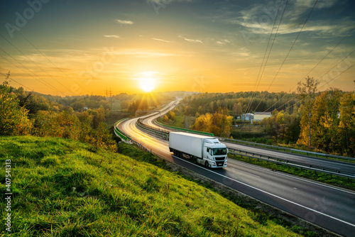 Fototapeta White truck driving on the highway winding through forested landscape in autumn