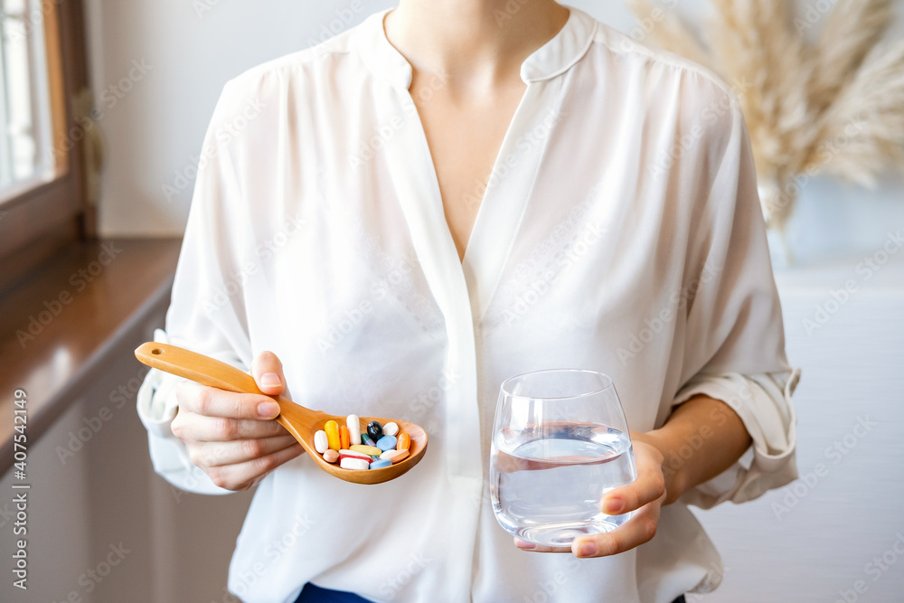 Woman in white blouse holding wooden spoon with multicolored pills supplements. Homeopathic therapy, naturopathy. Bioactive additive woman pharmacy. Vitamin mineral treatment. Health care concept Woman in white blouse holding wooden spoon with multicolored pills supplements. Homeopathic therapy, naturopathy. Bioactive additive woman pharmacy. Vitamin mineral treatment. Health care concept