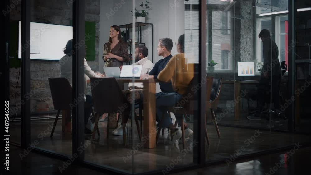 Project Manager Makes a Presentation for a Young Diverse Creative Team in Meeting Room in an Agency. Colleagues Sit Behind Conference Table and Discuss Business Development, Sales Analysis and Design.