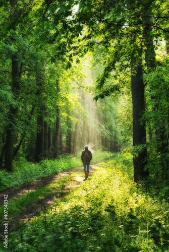 young woman walking along a forest trail with rays of sunlight shining through the leaves of the trees
