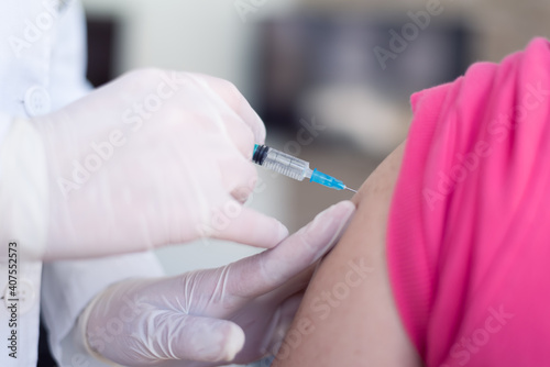 Young Female doctor in protective mask injecting or prepairing for injecting vaccine against coronavirus or ncov 19 or covid into patient's arm