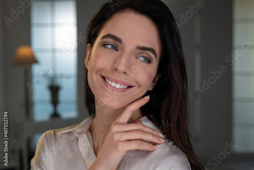 Beauty shot of happy young woman with perfect face skin after applying moisturizing cream is touching it gently with hand to show how soft and smooth it is. Concept of skincare, cosmetics, healthcare.
