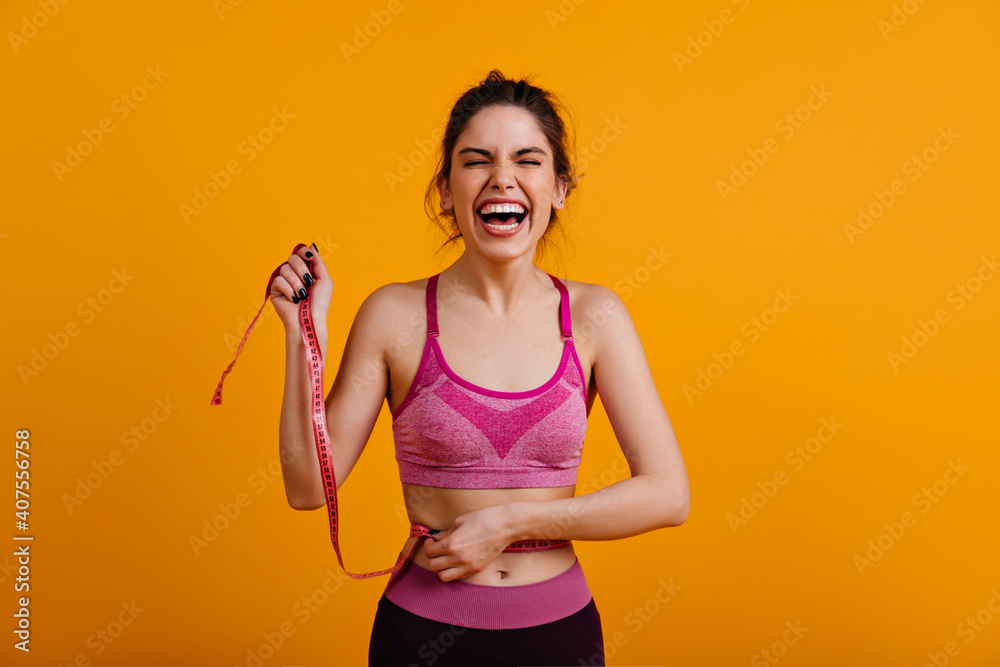 Merry european girl enjoying diet. Studio photo of fitness female model with measure tape.