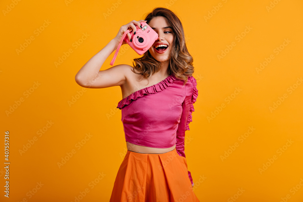 Curly brown-haired woman making photos with smile. Indoor shot of graceful girl wears pink blouse. Curly brown-haired woman making photos with smile. Indoor shot of graceful girl wears pink blouse.