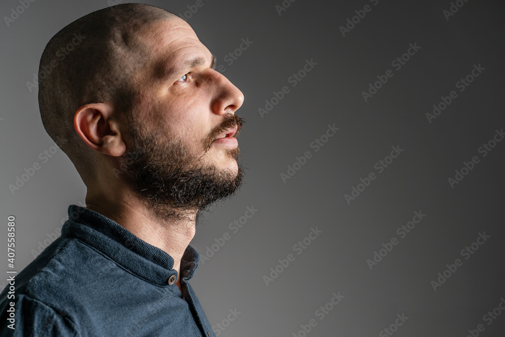 Fototapeta premium Side view close up portrait of adult caucasian man with beard and short hair looking up thoughtful with copy space - studio shot