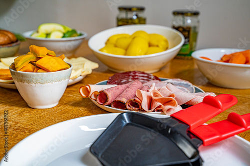 Detail photograph of a French raclette with all the typical ingredients, varieties of French cheeses, boiled potatoes, carrots, mushrooms, mushrooms, cucumbers and sausages, under natural light 