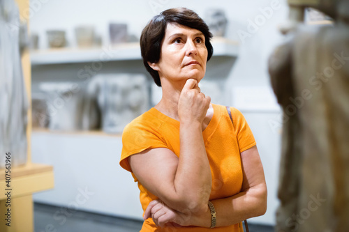 Obraz na plátne Thoughtful middle aged glad cheerful smiling lady examining exposition in museum hall of ancient sculpture