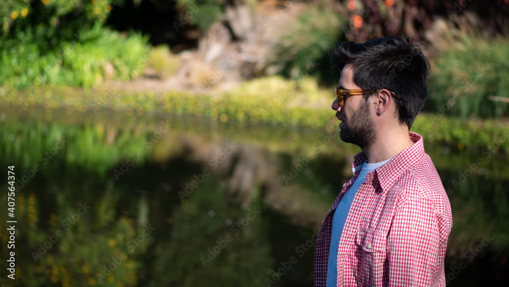 Young man standing nex to a pond wearing sunglasses Young man standing nex to a pond wearing sunglasses