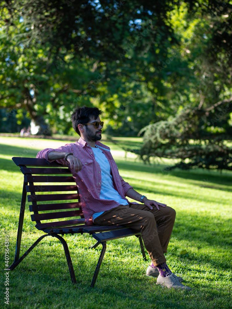 Young man sitting in a bank at the park using sun glasses Young man sitting in a bank at the park using sun glasses