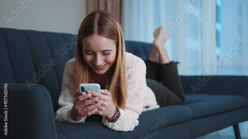 Slow motion happy young woman lying on sofa using smartphone in modern room. Social media. Relax. Tapping, scrolling. Internet online connection. Close up