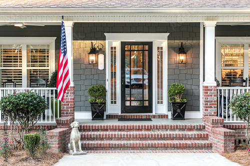 Front door entrance to a large two story blue gray house with wood and vinyl siding and a large American flag.