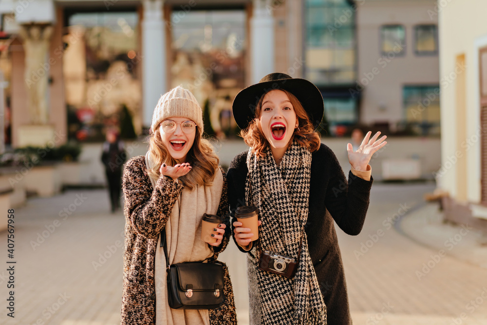 Obraz premium Caucasian girls expressing excitement while drinking coffee. Good-humoured friends walking together in good autumn day.