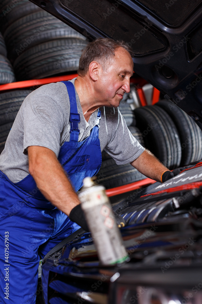 Elderly man mechanic engaged in car repair in modern auto workshop..