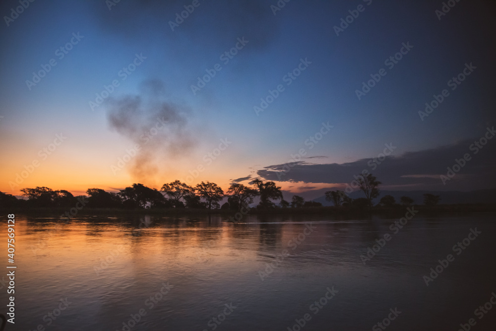 Smoke rising from a village along African river at sunset