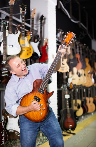 happy male is playing on electric guitar and satisfied it in music store.