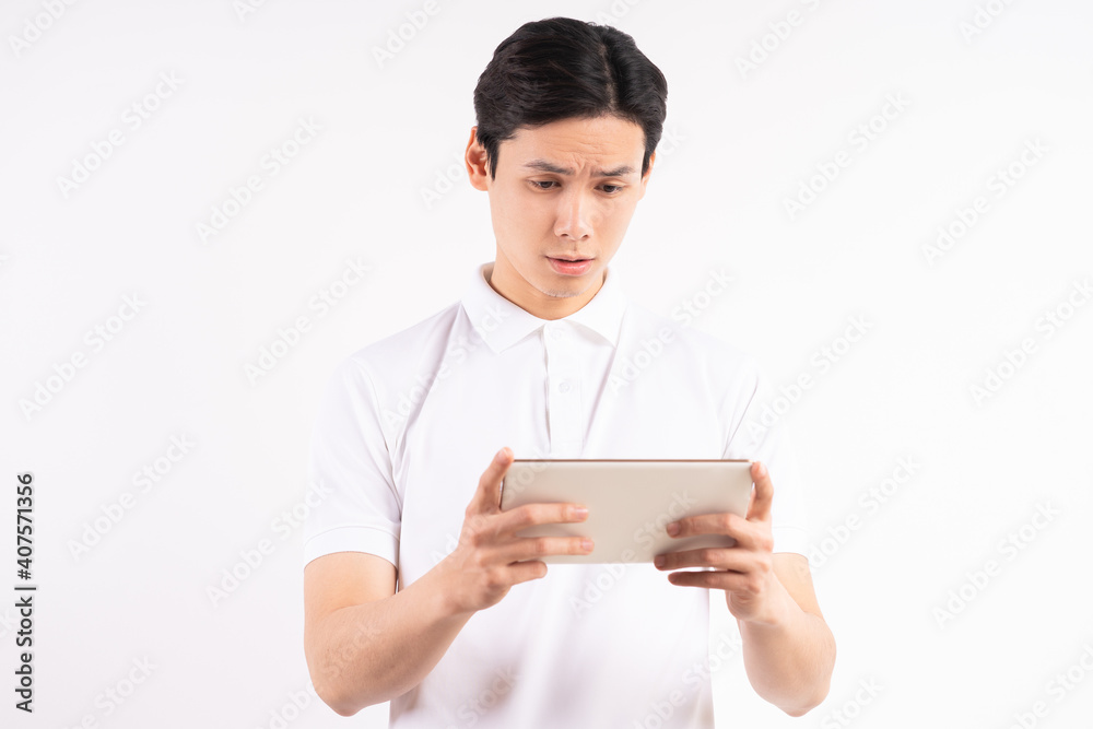 Cheerful young man standing on isolated white wall background. Stared at the tablet Cheerful young man standing on isolated white wall background. Stared at the tablet