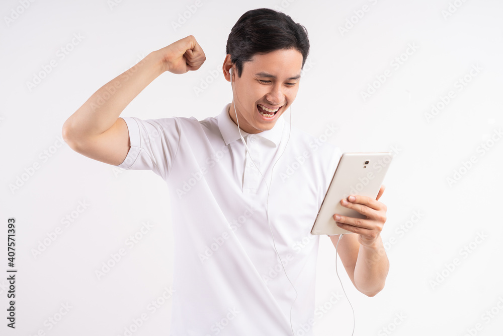 Image of happy young man standing on isolated white wall background. Look aside using the tablet as a winner gesture. Image of happy young man standing on isolated white wall background. Look aside using the tablet as a winner gesture.