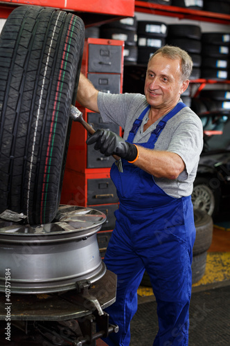 Elderly man mechanic engaged in repair of car wheel in auto workshop.. © JackF