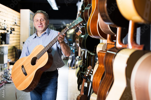 Smiling adult guitarist is holding modern acoustic guitar in music store