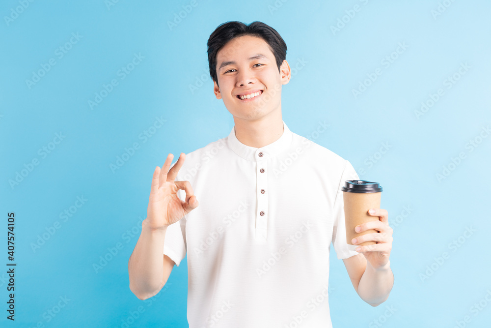 A photo of a handsome Asian boy holding a paper cup in his hand and using an ok symbol A photo of a handsome Asian boy holding a paper cup in his hand and using an ok symbol