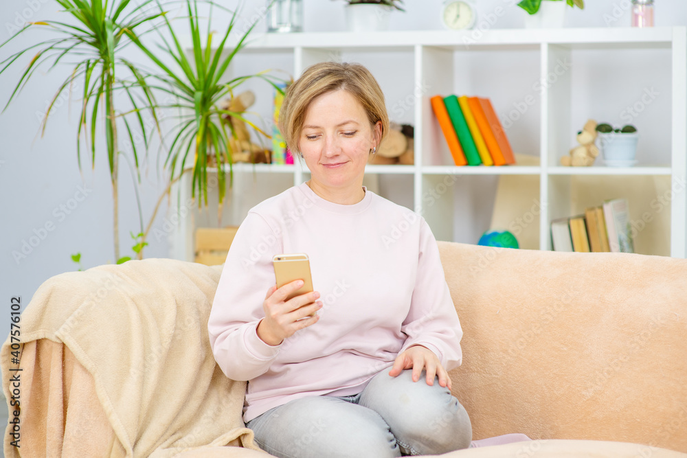 Young woman sitting on sofa at home with phone in hand and looking at phone screen Young woman sitting on sofa at home with phone in hand and looking at phone screen