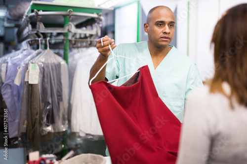 Positive man laundry worker returning clean clothes to customer at dry-cleaning facility