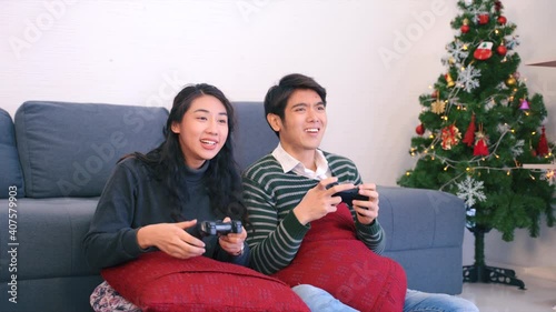 Asian young couple escape from cold wind in winter by sitting on couch in living room enjoy playing video games. Happy couple play video games at home husband and wife smile and laugh enjoying.