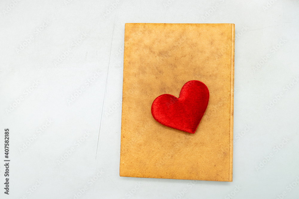 A red heart placed on an orange notebook on a white background A red heart placed on an orange notebook on a white background