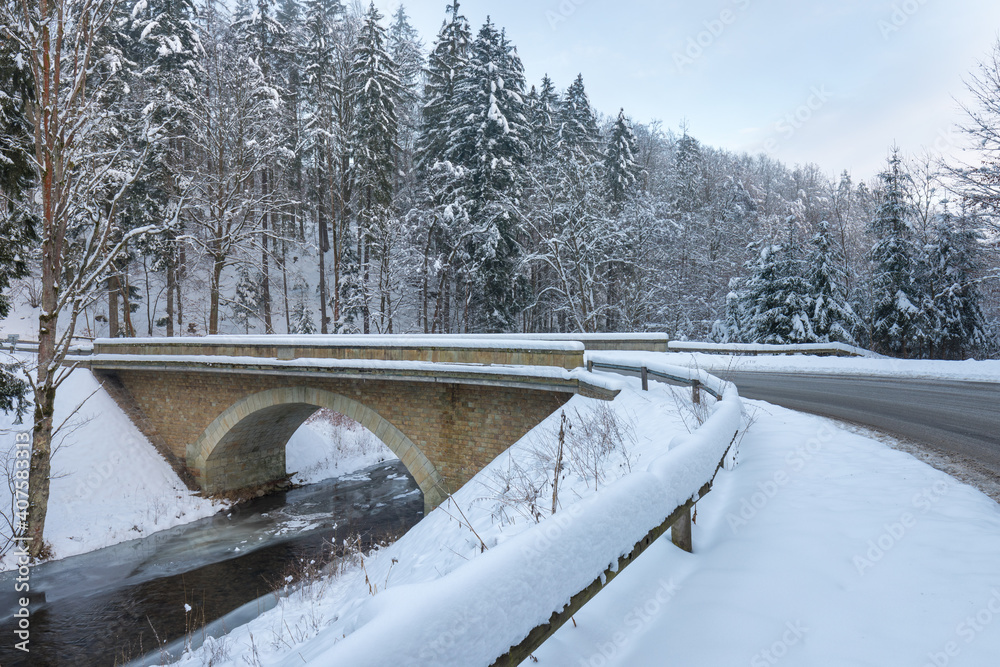 Wild river in winter with old stone arched bridge.
Beautiful frosty day. Snowy weather in mountain. Most popular place. Alps mountains.