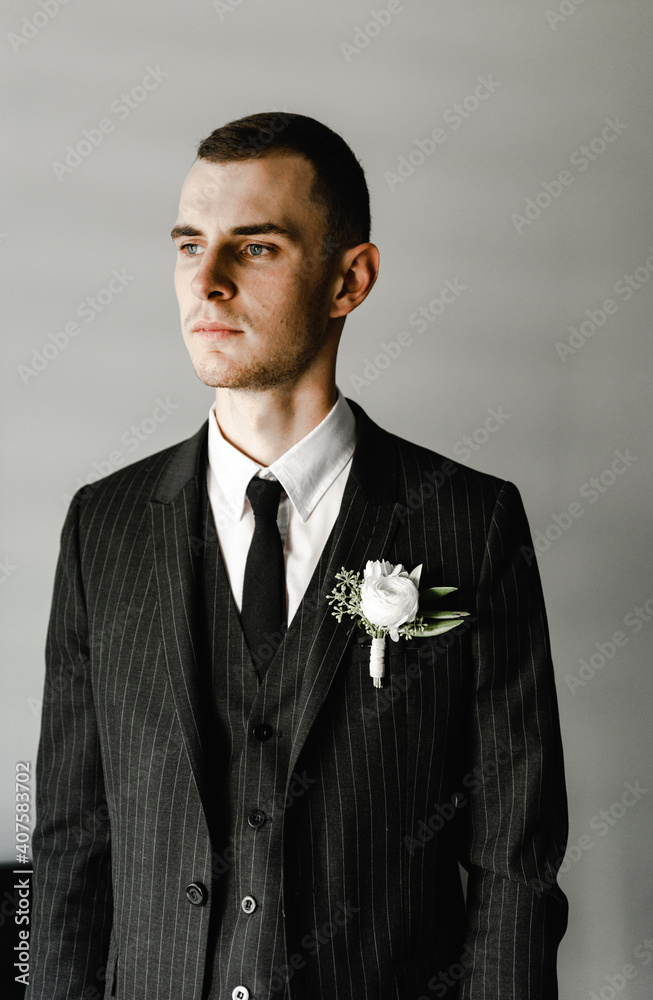 groom in a black suit stands against the gray background of his room. fees of the groom. wedding day. the groom is nervous before the wedding ceremony groom in a black suit stands against the gray background of his room. fees of the groom. wedding day. the groom is nervous before the wedding ceremony