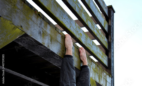 young man hangs on a wooden railing and tries to step up, his hand slides and he clings to the rescuer. he climbs into the apartment due to a robbery, an assault, he forgets the keys to mistrress photo