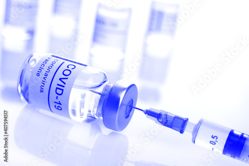 Glass vial with coronavirus vaccine label along with syringe closeup toned blue photo