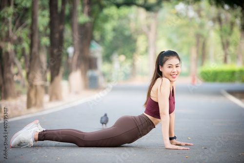 Asian Young female workout before fitness training session at the park. Healthy young woman warming up outdoors. She is stretching her arms and Leg stretching