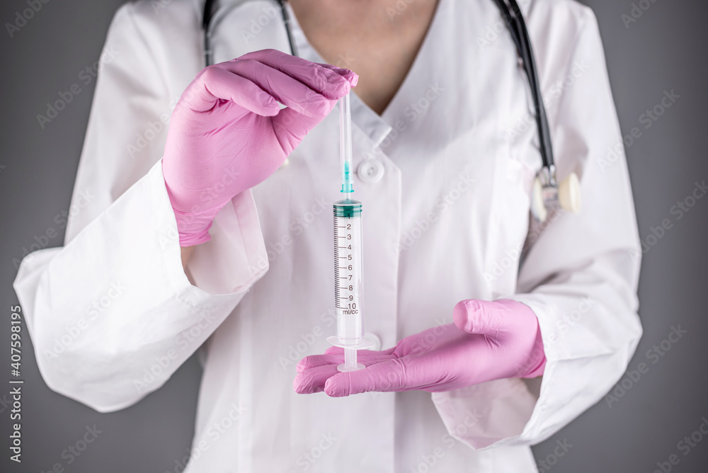 A female doctor in a white lab coat and pink gloves is holding a syringe. Concept of health care and vaccination. Closeup A female doctor in a white lab coat and pink gloves is holding a syringe. Concept of health care and vaccination. Closeup