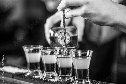 Shots at the nightclub. Red cocktail at the nightclub. Barman preparing cocktail shooter. Bartender pouring strong alcoholic drink into small glasses on bar. Black and white photo